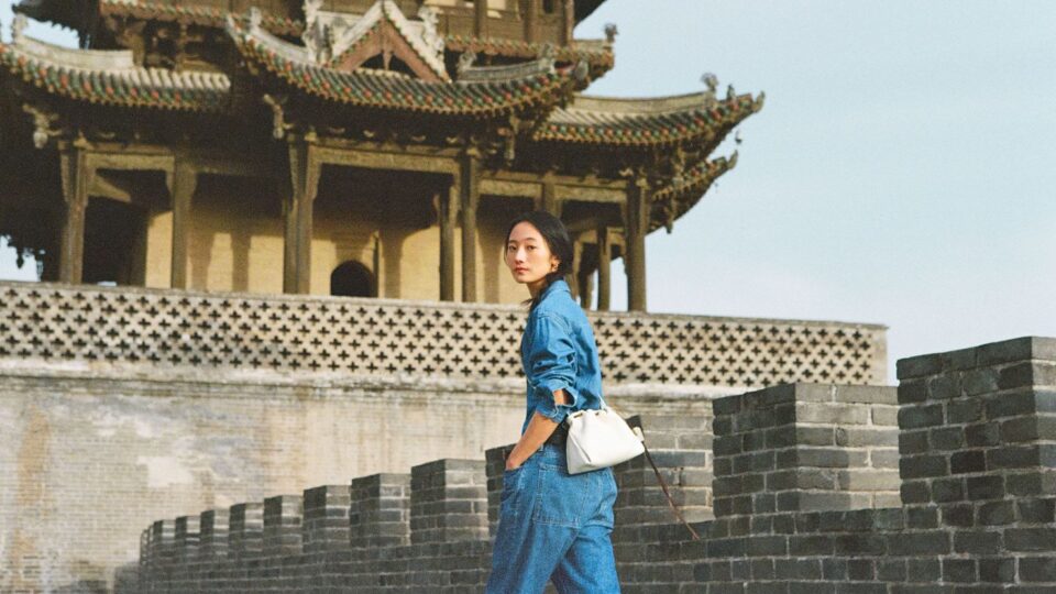 A model in a recent campaign  by Chinese luxury brand Songmont wearing a chic, minimalist outfit and handbag outside a temple in China.