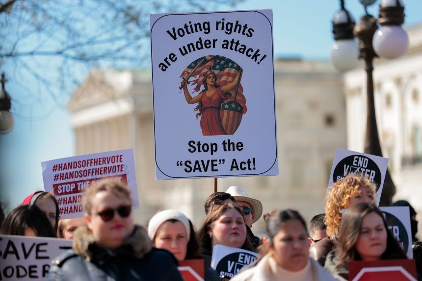 Attendees hold signs during a rally against the SAVE America Act at a rally outside the US Capitol on March 18, 2026.