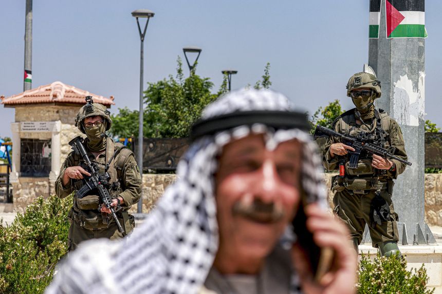 gettyimages-2283320497-1 A Palestinian man speaks on a phone near Israeli army soldiers standing guard at the archaeological site of Sebastia on June 29.