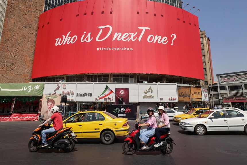 gettyimages-2286118246 Motorcyclists ride past a huge anti-US billboard referring to the death of US Senator Lindsey Graham at Valiasr Square in Tehran on July 19. The United States said airstrikes on July 19 aimed to "punish" Iran over the first US military deaths since renewed hostilities with the Islamic republic.