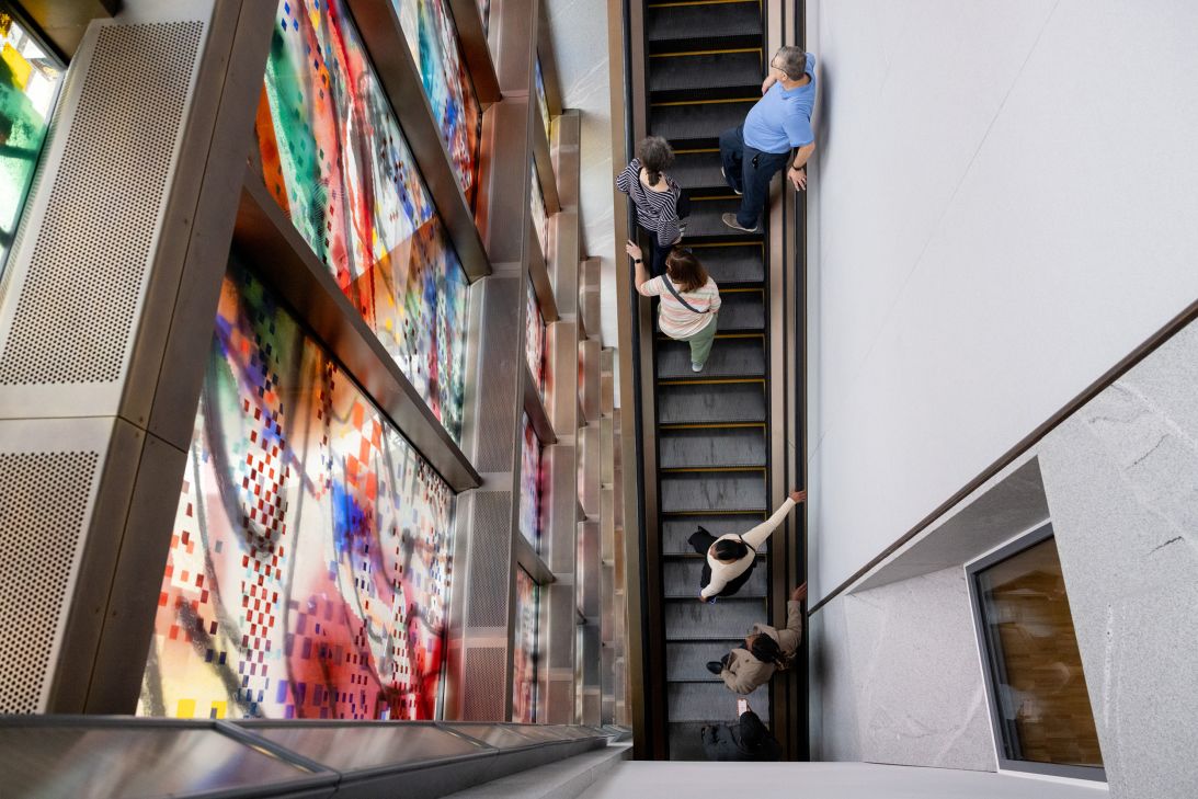 Visitors on the escalator take in Julie Mehretu’s painted vertical window, “Uprising of the Sun,” which stretches up multiple floors.